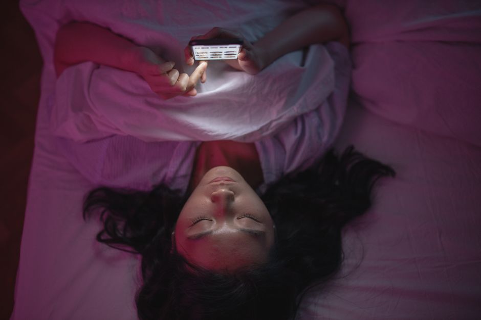 Smartphone allumé dans le noir à côté d'un lit, visage éclairé par la lumière bleue